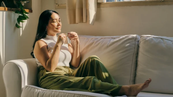 A woman seated on a couch, drinking a coffee, appearing content.
